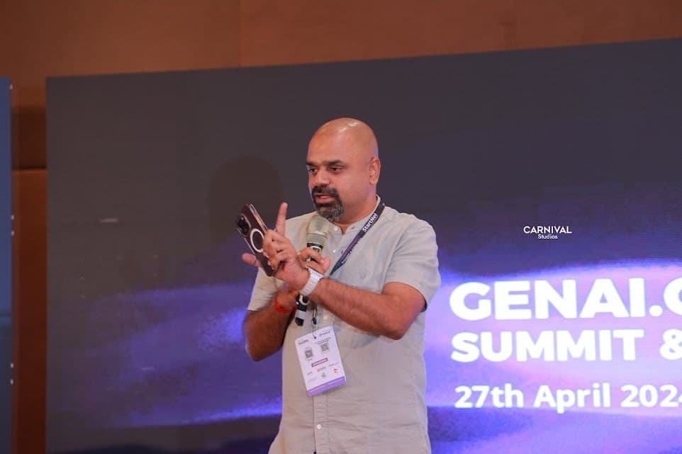 Maran speaking at the GenAI Connect Summit, microphone in one hand and phone in the other