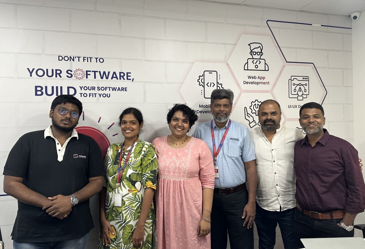 Maran with six colleagues in front of an office wall reading “Don’t fit to your software, build your software to fit you”