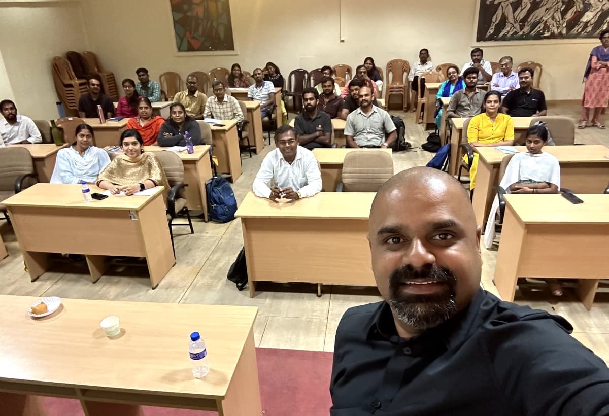 Maran taking a selfie in a training room with around thirty seated participants behind him